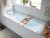 Helle Badewanne aus der Geberit Renova Plan Serie mit Wandarmatur und Holzablage.